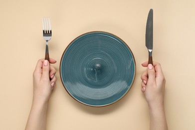 Photo of Woman holding fork and knife near empty plate at beige table, top view