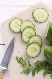 Cucumbers, dill, knife and marble cutting board on white wooden table, top view