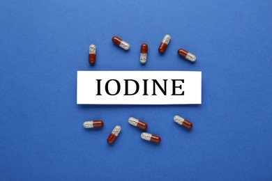 Photo of Card with iodine element and pills on blue background, flat lay