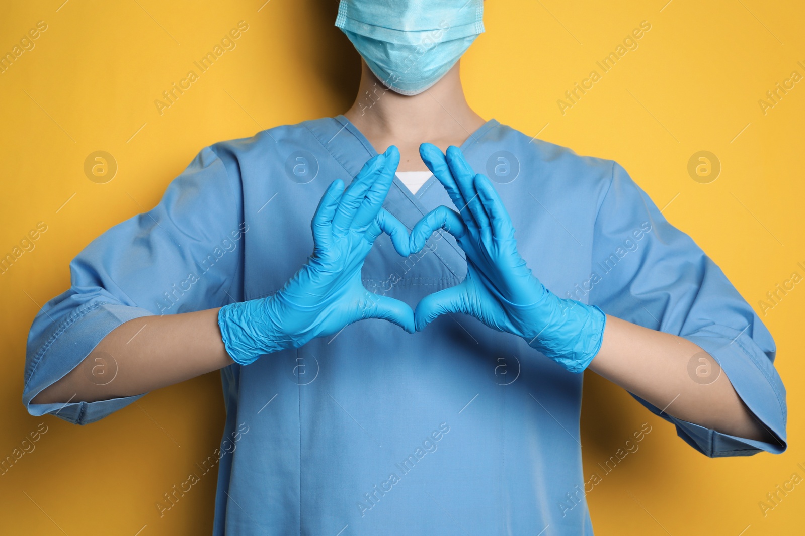 Photo of Doctor making heart with hands on yellow background, closeup