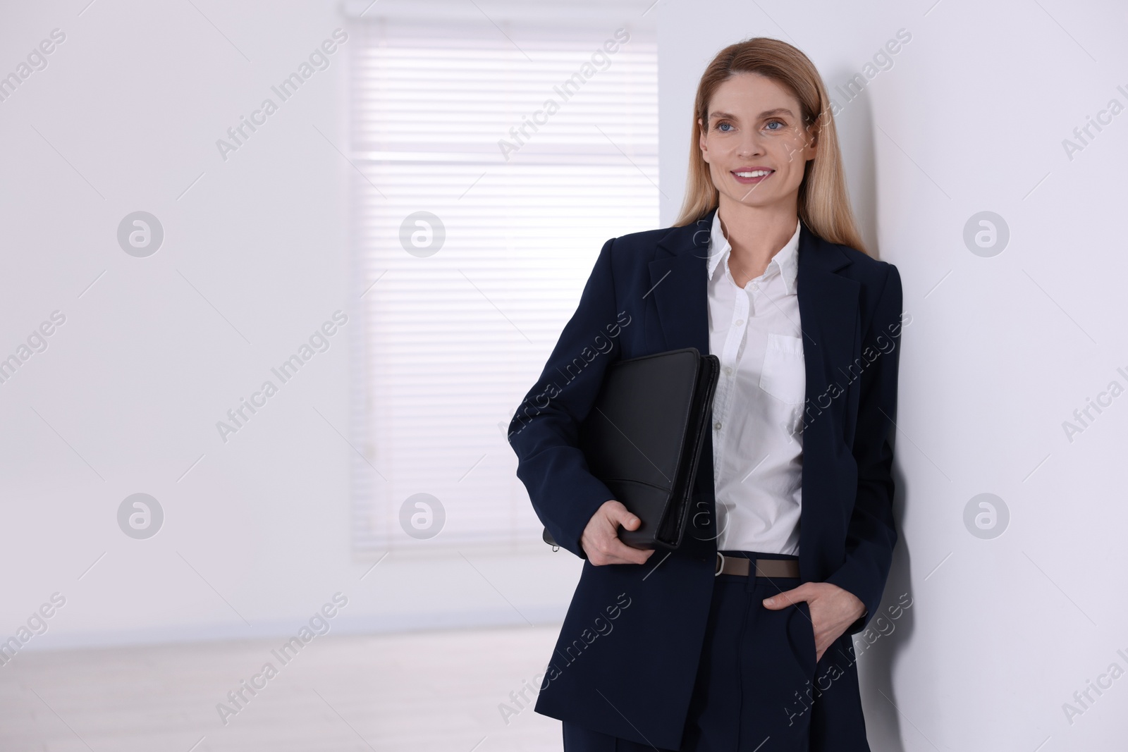 Photo of Happy real estate agent with leather portfolio indoors. Space for text