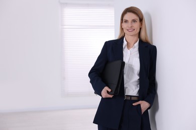 Photo of Happy real estate agent with leather portfolio indoors. Space for text