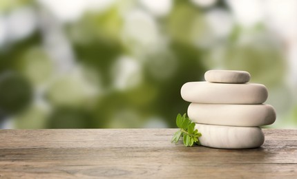 Image of Stack of spa stones and green branch on wooden table against blurred green background, space for text