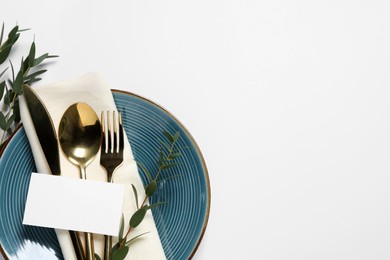 Stylish table setting with cutlery, blank card and eucalyptus leaves on white background, top view. Space for text