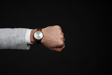 Photo of Businessman wearing wristwatch on black background, closeup. Time management