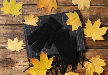 Flat lay composition with stylish black woolen gloves and dry leaves on wooden table