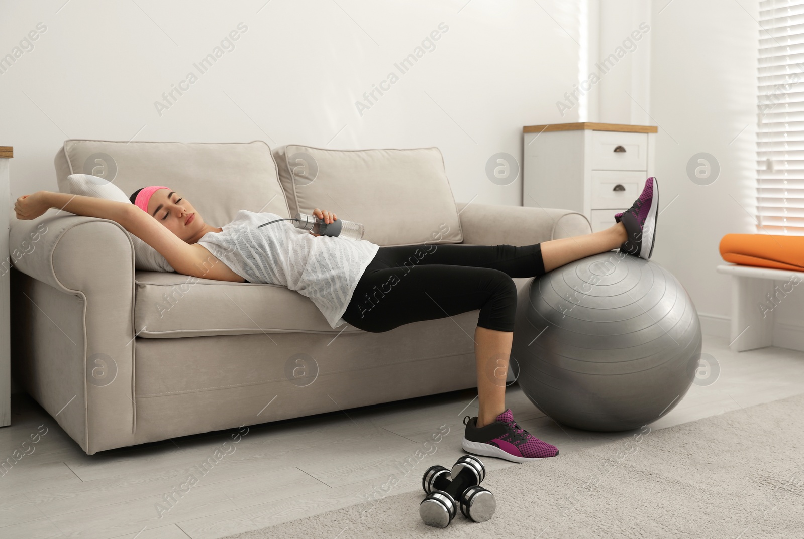 Photo of Lazy young woman with sport equipment on sofa at home