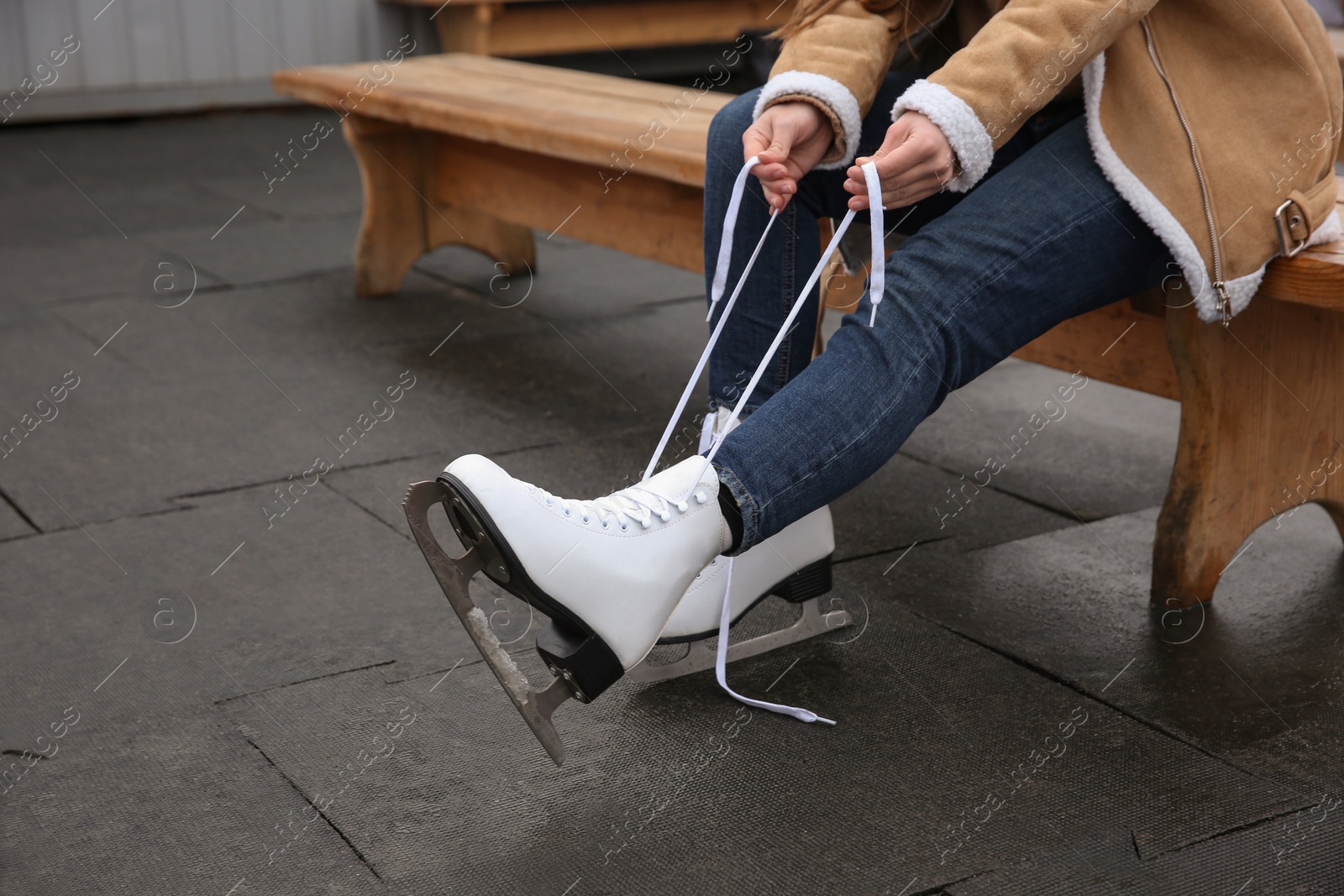 Photo of Woman lacing figure skate while sitting on bench, closeup