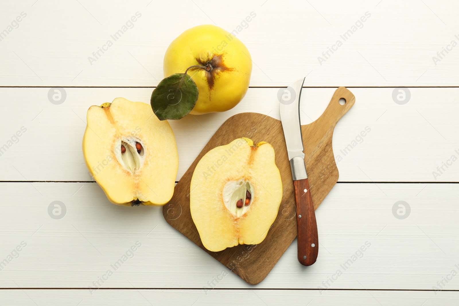 Photo of Tasty ripe quince fruits and knife on white wooden table, flat lay