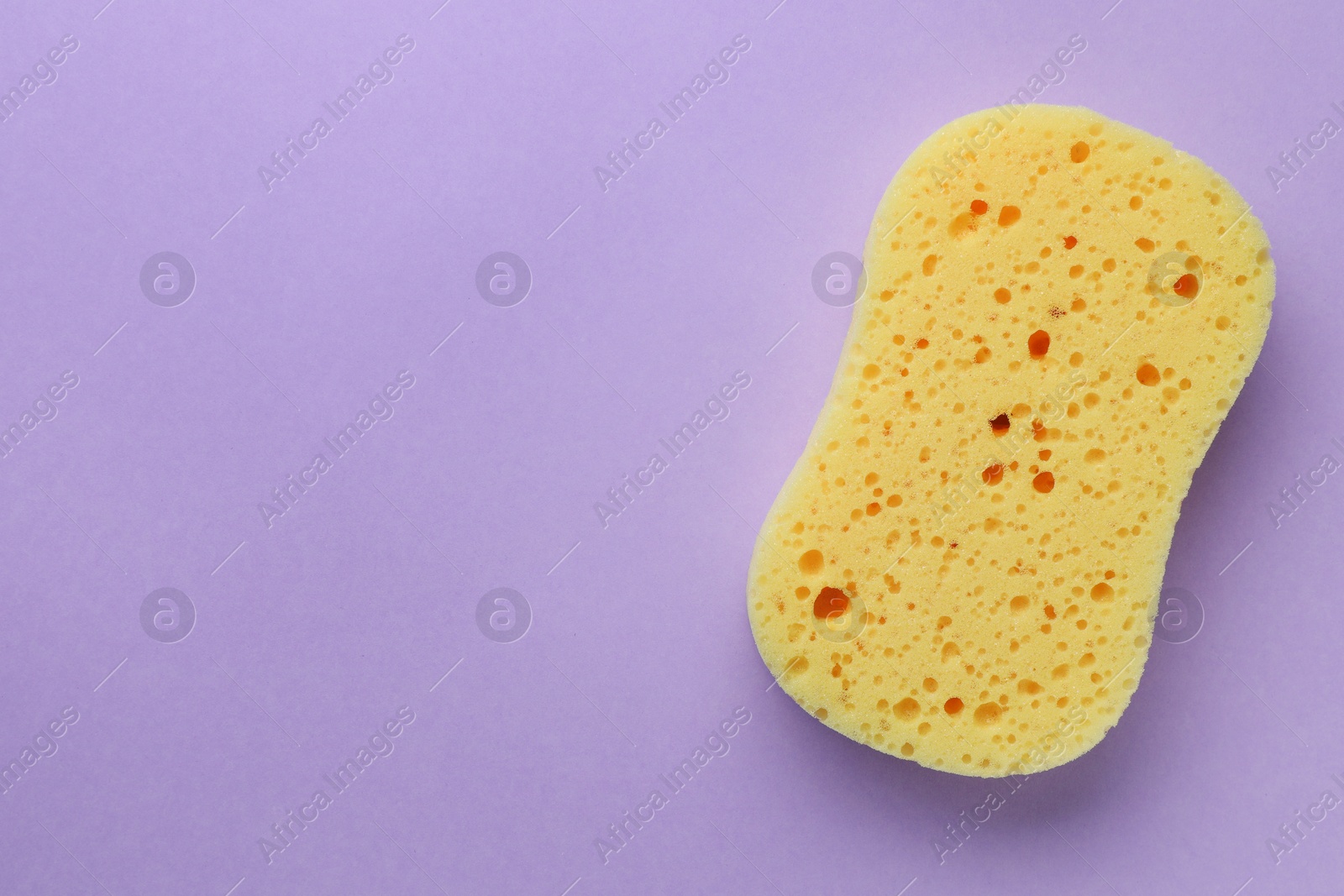 Photo of New yellow sponge on violet background, top view. Space for text