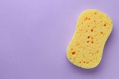 New yellow sponge on violet background, top view. Space for text