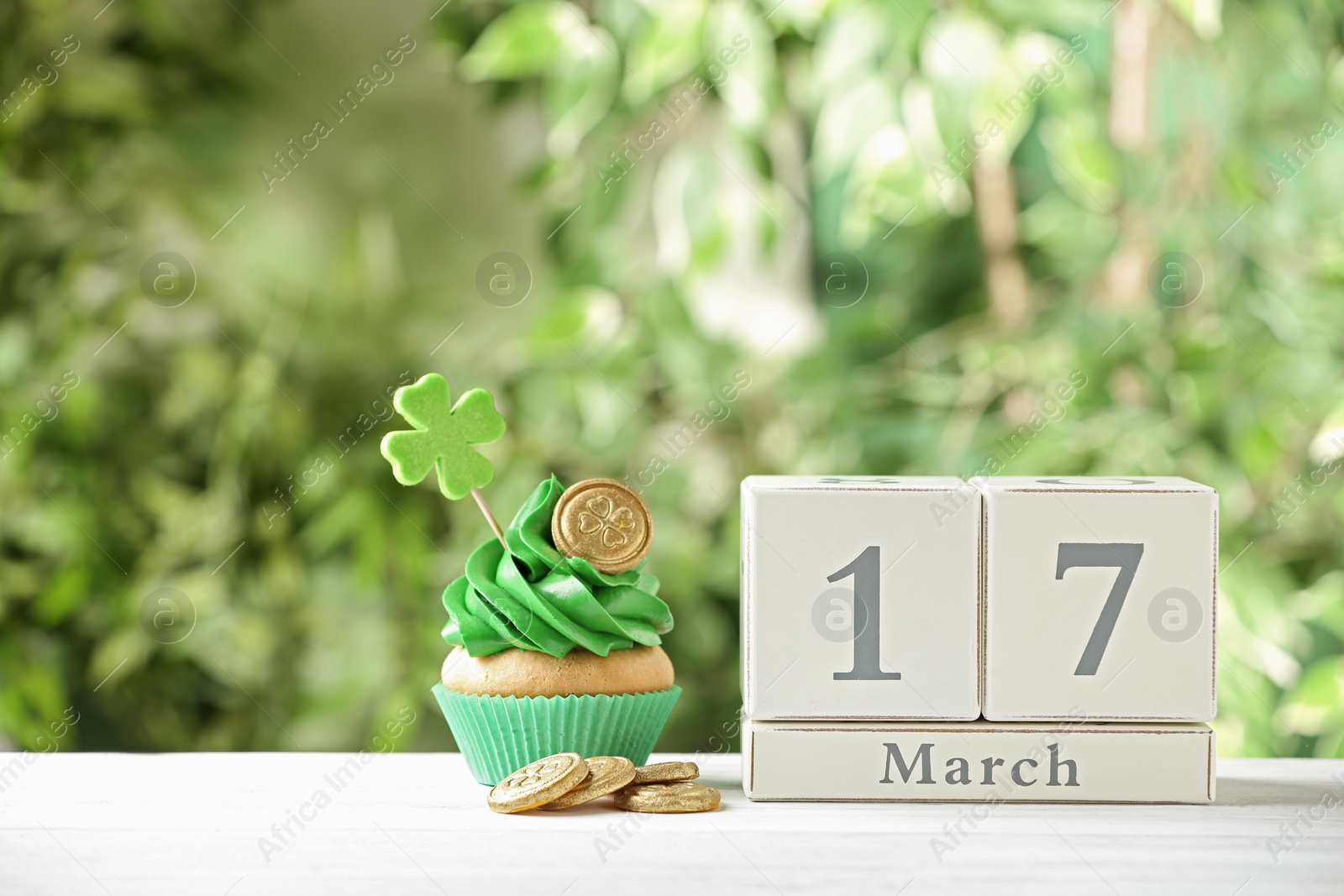 Photo of Composition with block calendar on white wooden table against blurred greenery. St. Patrick's Day celebration