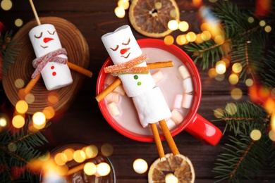 Image of Flat lay composition with funny marshmallow snowman in cup of hot drink on wooden table. Bokeh effect 
