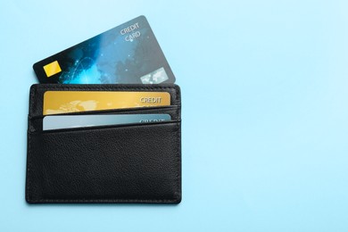 Photo of Leather card holder with credit cards on light blue background, top view. Space for text