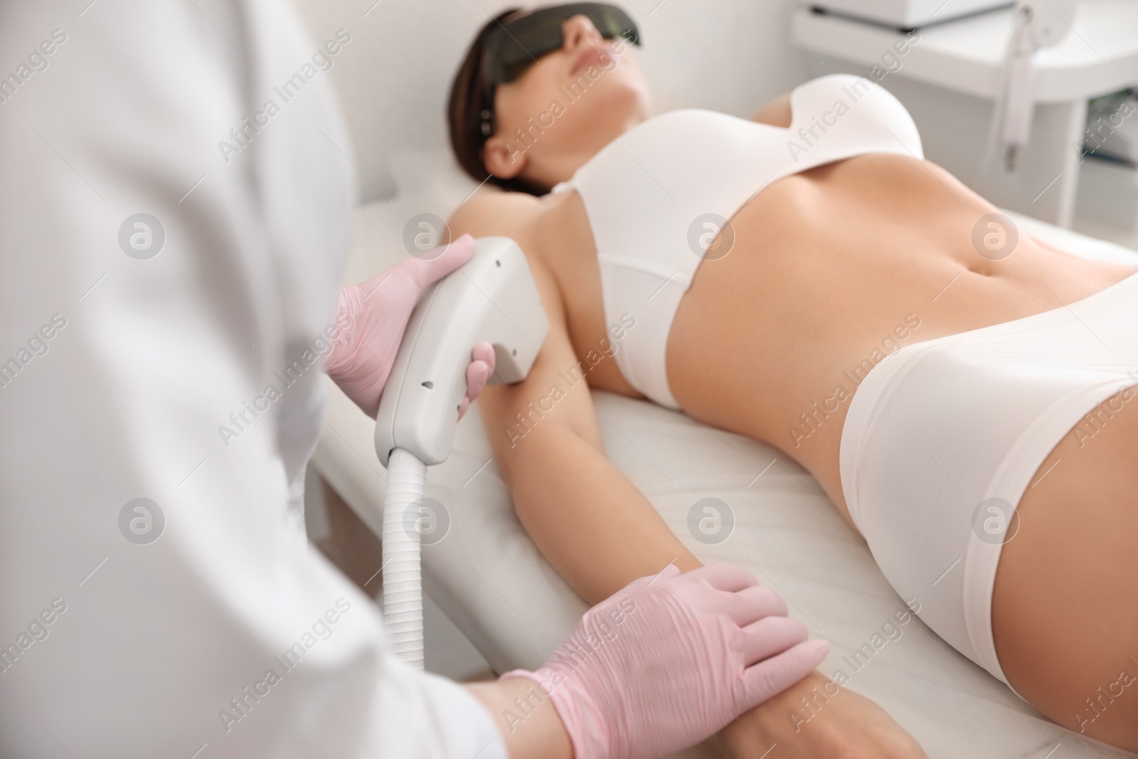 Photo of Young woman undergoing laser epilation procedure in beauty salon, focus on hands