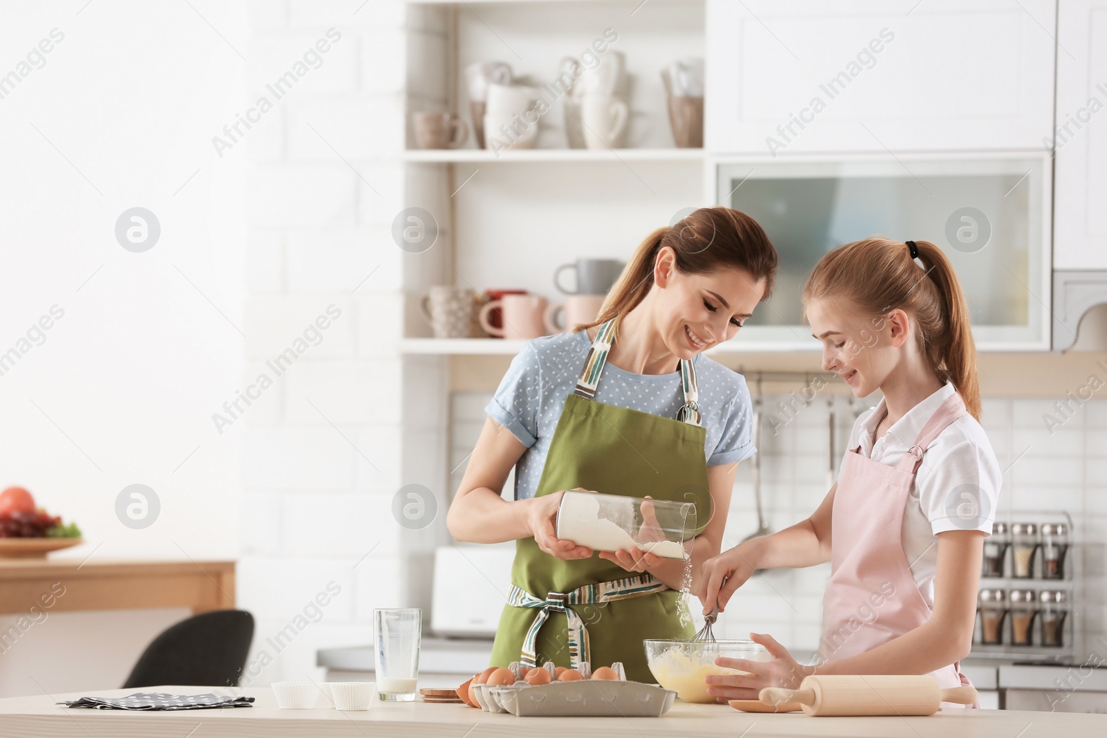 Photo of Mother and her daughter making dough at table in kitchen