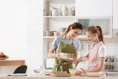 Photo of Mother and her daughter making dough at table in kitchen