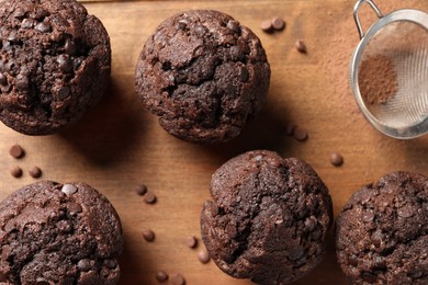 Delicious chocolate muffins and sieve with cocoa powder on wooden table, flat lay