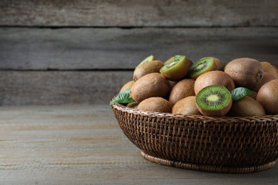 Fresh ripe kiwis in wicker bowl on wooden table, space for text