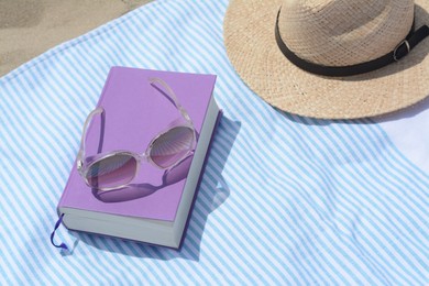 Beach towel with book, sunglasses and straw hat on sand