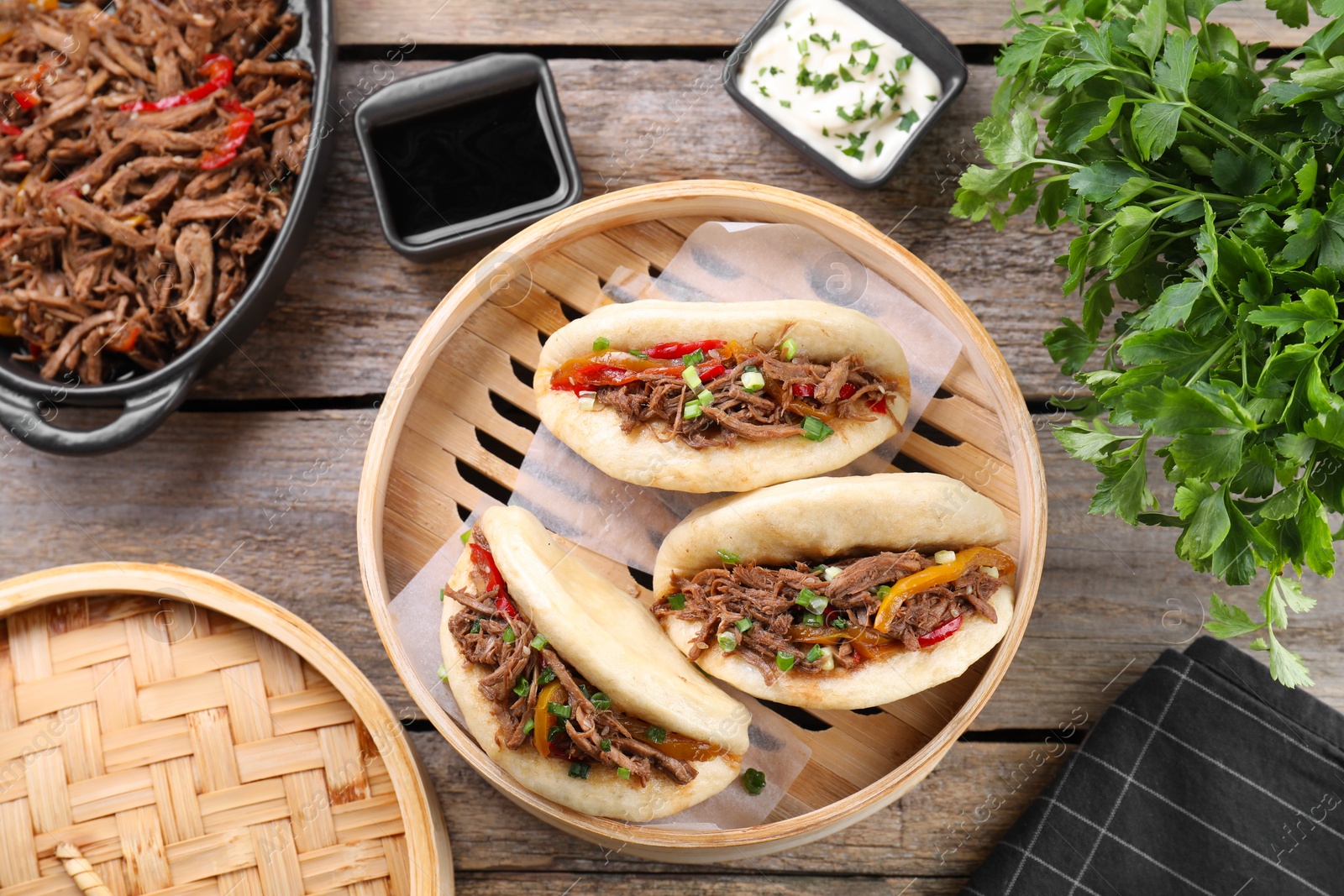 Photo of Delicious gua bao in bamboo steamer on wooden table, flat lay