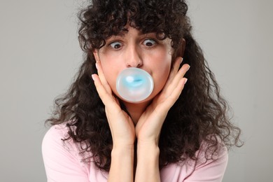 Beautiful young woman blowing bubble gum on grey background