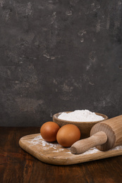 Photo of Raw eggs, flour and rolling pin on wooden table. Baking pie
