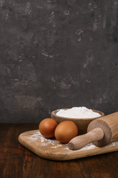 Raw eggs, flour and rolling pin on wooden table. Baking pie