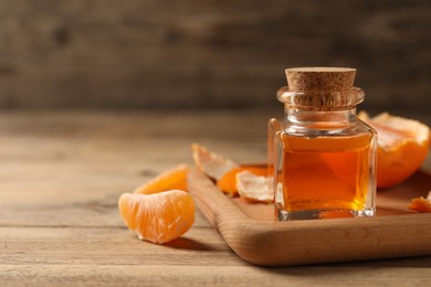 Bottle of tangerine essential oil and peeled fresh fruit on wooden table, closeup. Space for text