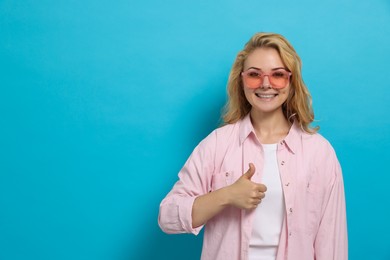 Photo of Happy young woman showing thumb up gesture on light blue background. Space for text