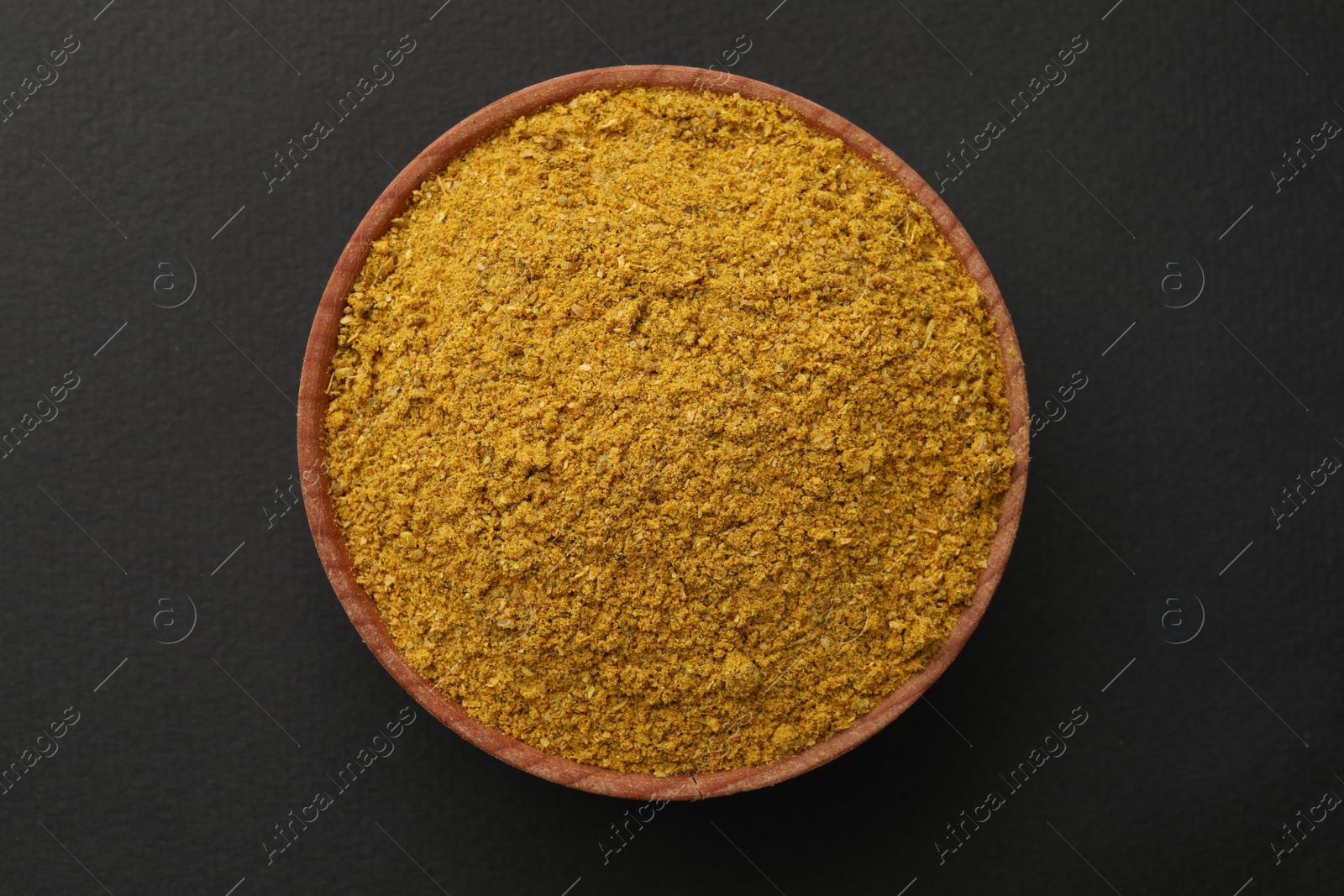 Photo of Wooden bowl with turmeric powder on dark background, top view