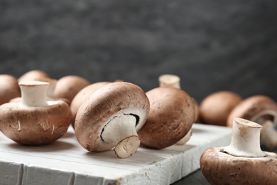 Photo of Fresh champignon mushrooms on wooden cutting board, closeup