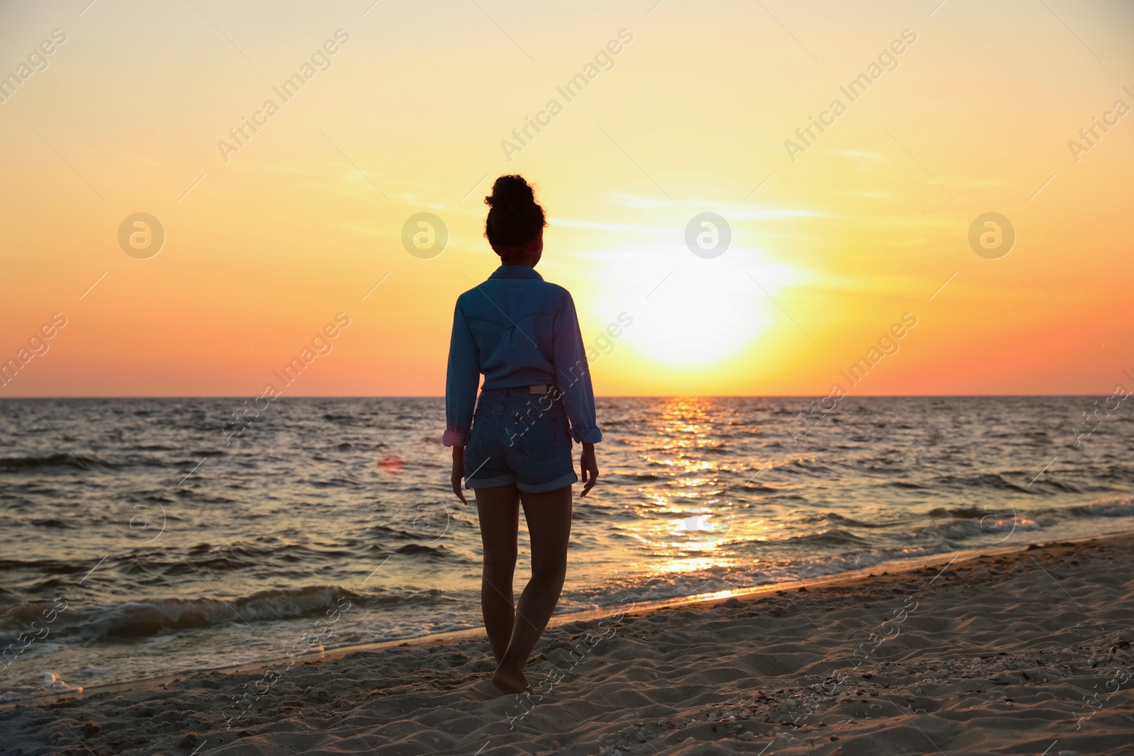 Photo of Girl on sandy beach near sea at sunset, back view