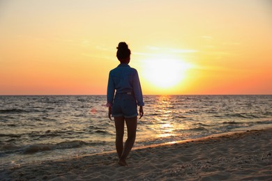 Girl on sandy beach near sea at sunset, back view