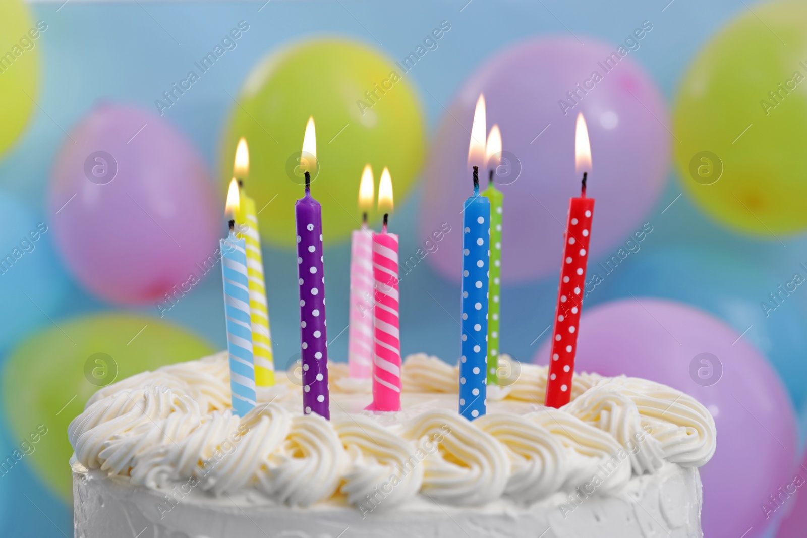 Photo of Delicious cake with burning candles and festive decor on light blue background, closeup