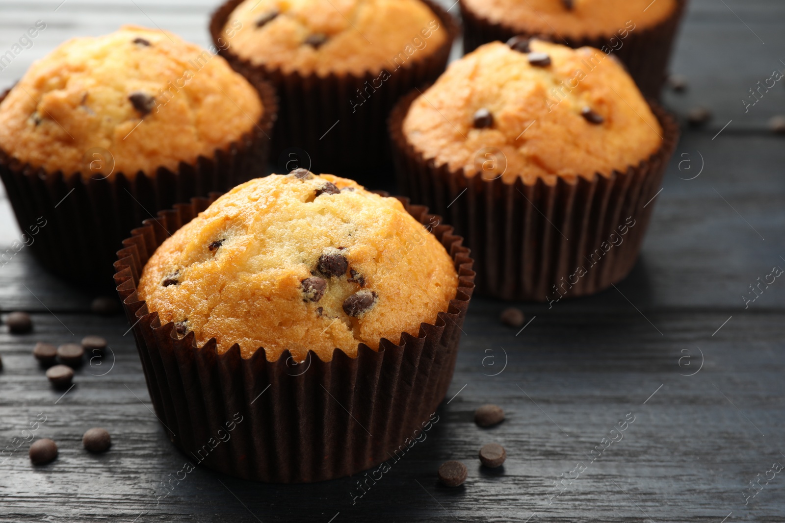 Photo of Delicious freshly baked muffins with chocolate chips on dark gray table, closeup