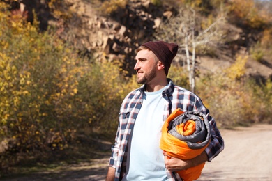 Photo of Young male camper with sleeping bag in wilderness