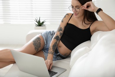 Photo of Beautiful woman with tattoos on body using laptop in living room