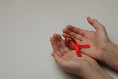 Little girl holding red ribbon on beige background, closeup with space for text. AIDS disease awareness
