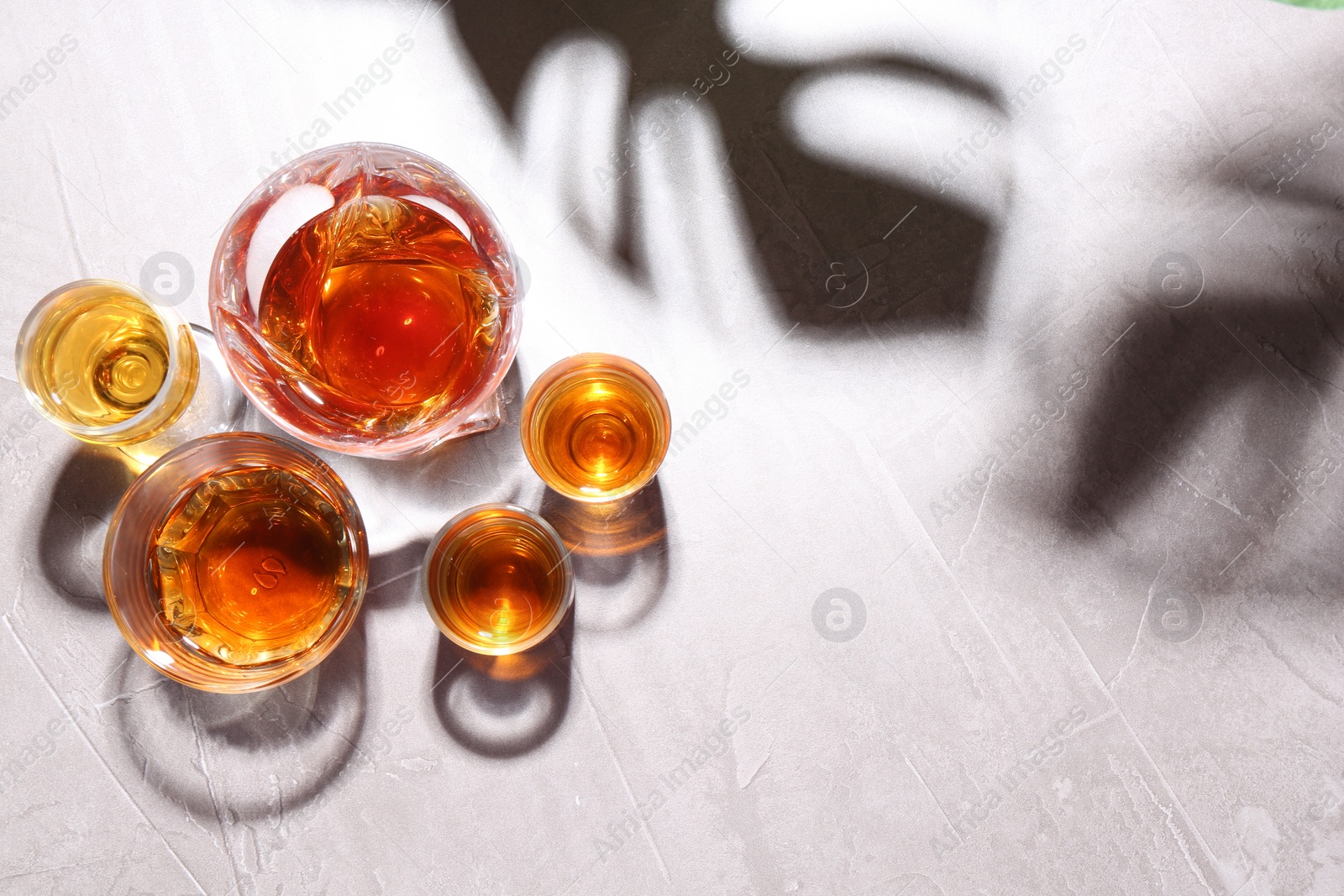 Photo of Many different liqueurs in glasses on light table, flat lay. Space for text