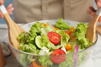 Photo of Woman preparing tasty fresh Greek salad in bowl at table, closeup