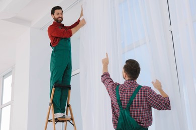 Workers in uniform hanging window curtain indoors