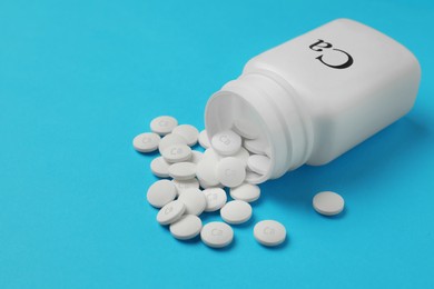 Photo of Overturned bottle of calcium supplement pills on light blue background, space for text