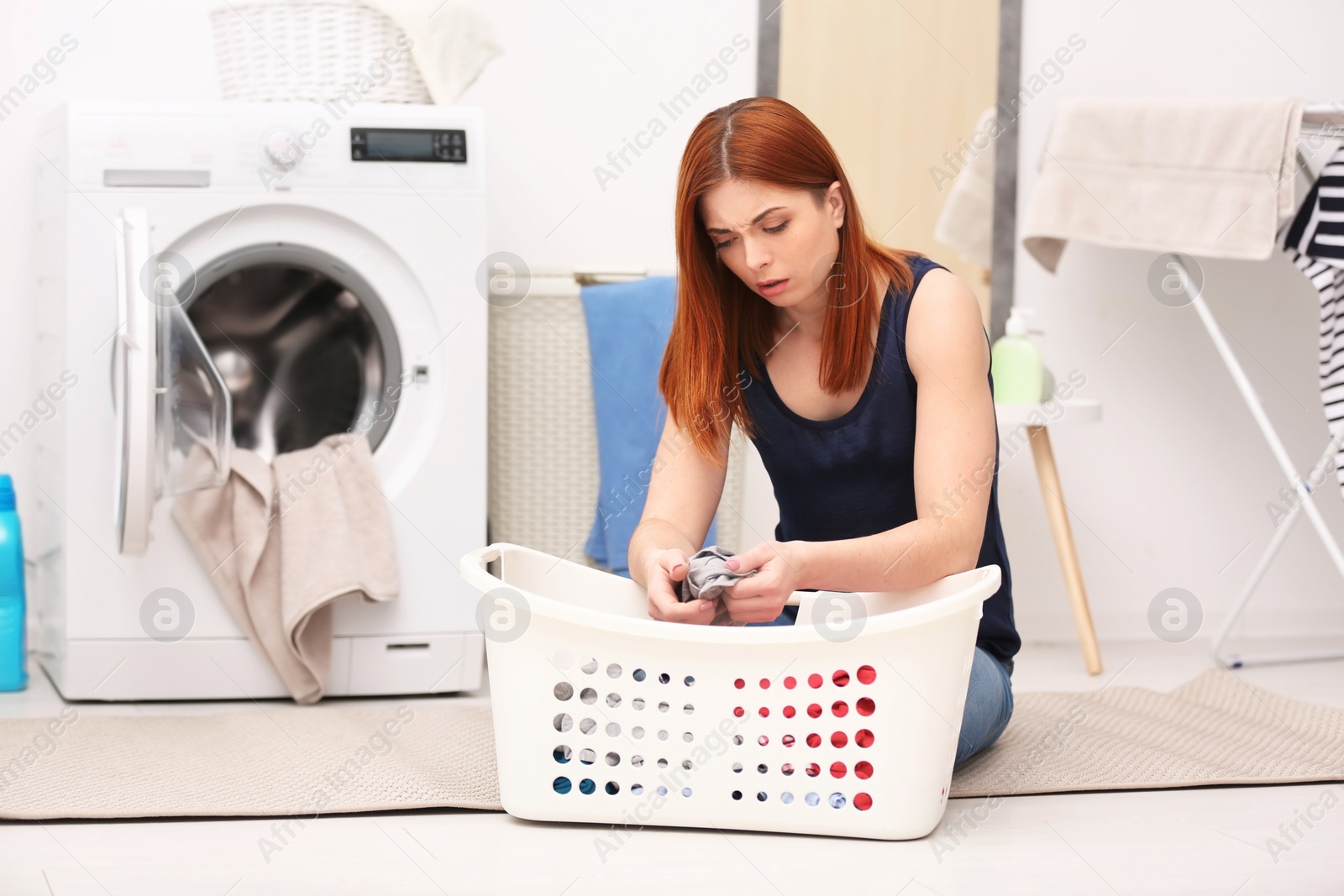 Photo of Tired housewife with basket of clothes in laundry room