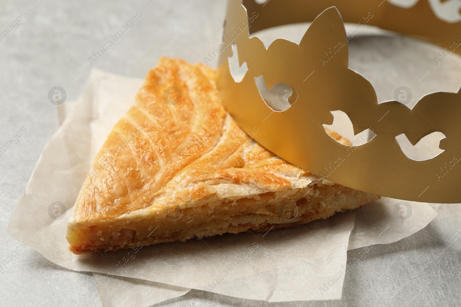Photo of Slice of traditional galette des Rois with paper crown on light grey table, closeup