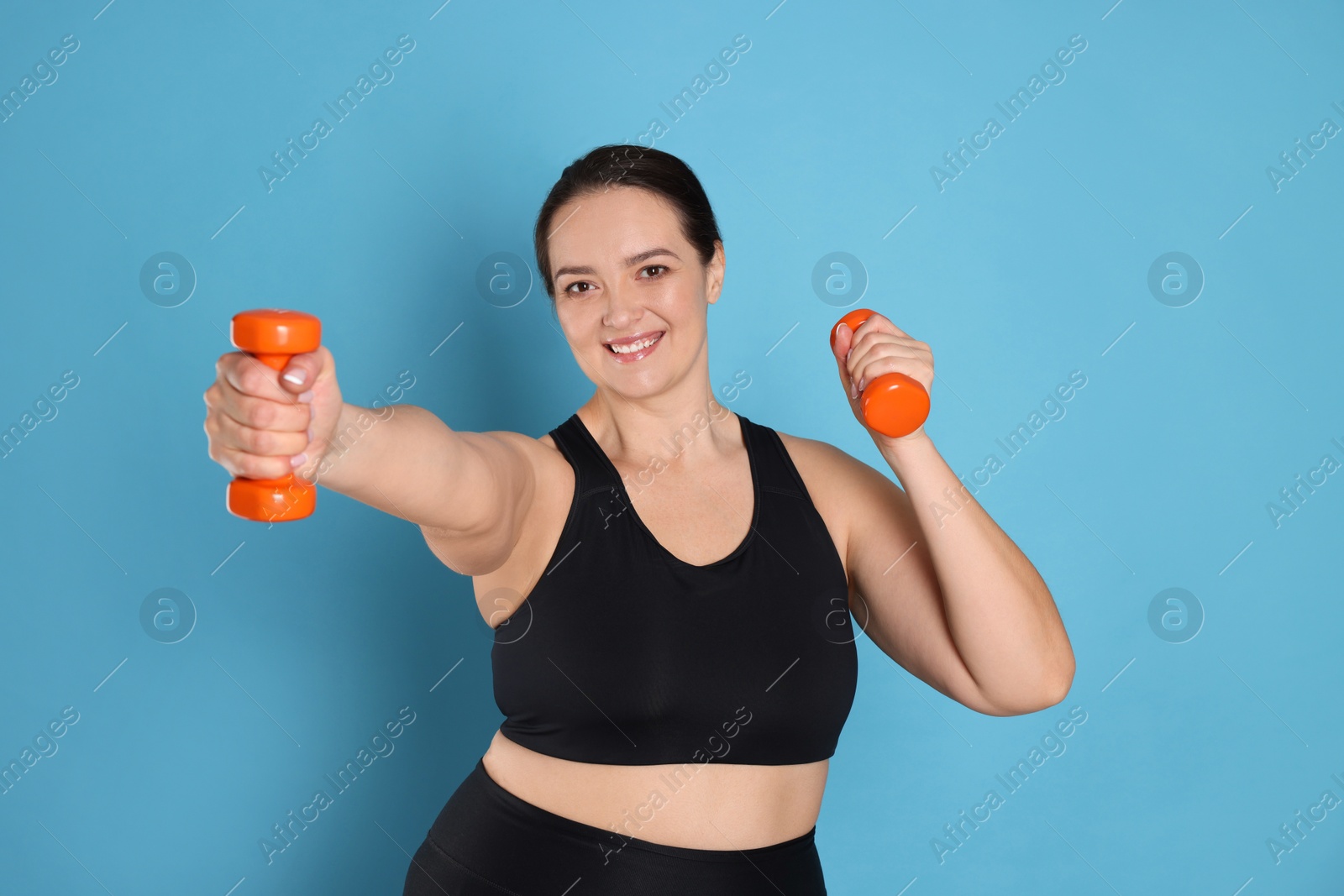 Photo of Happy overweight woman doing exercise with dumbbells on light blue background