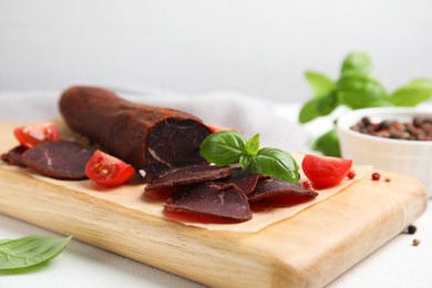 Photo of Delicious dry-cured beef basturma with basil and tomatoes on white table, closeup