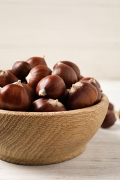 Photo of Fresh sweet edible chestnuts in bowl on white wooden table, closeup