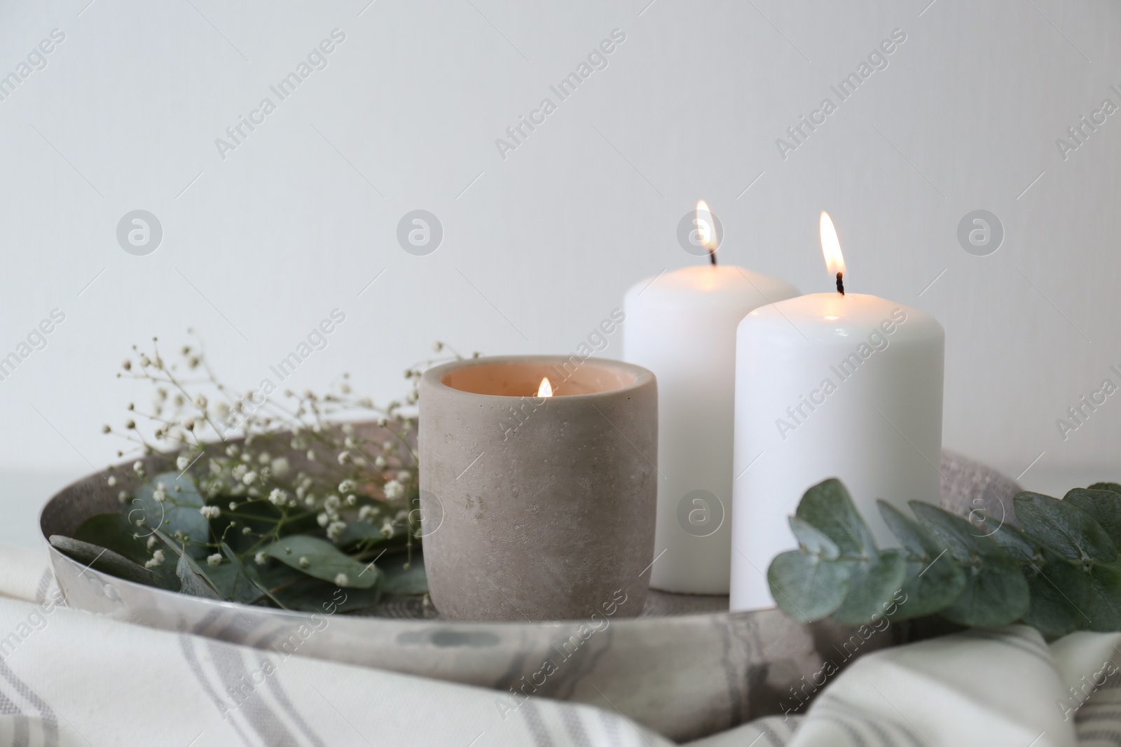 Photo of Beautiful eucalyptus branches, flowers and burning candles on fabric, closeup. Interior element