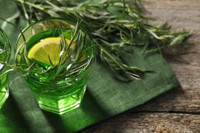 Glass of refreshing tarragon drink with lemon slice on wooden table. Space for text